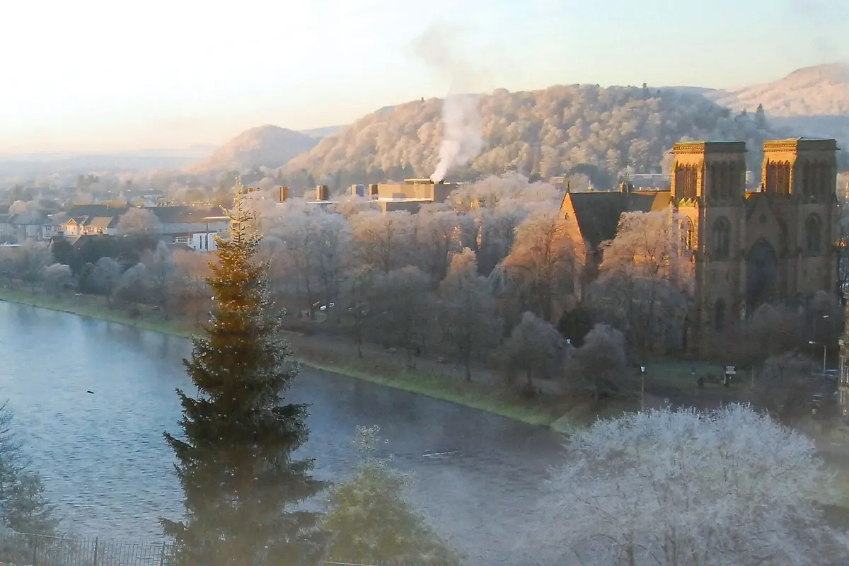 Dvojice věží katedrály v Invernessu se tyčí nad ojíněnými stromy u řeky Ness za zimního rána